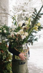 Person holding a vase of flowers with a snowy background