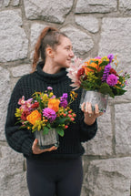 Person holding two floral arrangements against a stone wall