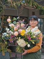Person holding a bouquet of flowers in front of a floral shop.
