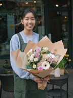 A smiling florist holding a custom soft pastel hand-tied bouquet outside the Senka Florist storefront in Whistler.