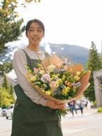Senka Florist team member holding a large, vibrant yellow and pastel hand-tied bouquet with the Whistler mountains in the background.